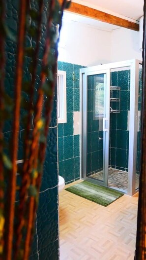 A glass-enclosed shower area with a wooden floor and a green mat.