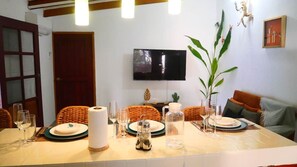 A dining area with a table set for four, a television mounted on the wall, and a door to the left. - Studio Tropical Jungle-Vue sur Mer/Pied dans l'eau (Libreville)