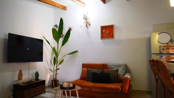 A living room with a sofa, a TV mounted on the wall, a plant, and a framed picture.