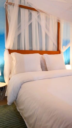 A bed with white bedding, a wooden headboard, and sheer curtains.
