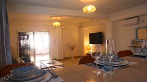 Un coin repas avec une table dressée pour quatre personnes, un téléviseur fixé au mur et une grande fenêtre.
