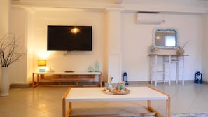 A living room with a flat-screen TV, a white coffee table, a sofa, and a small side table with decorative items.