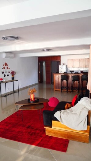 A modern living room with a red carpet, a wooden sofa, and a kitchen in the background.