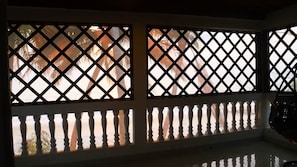 A room with a view through a lattice window, a balcony with balustrades, and a reflection on the floor.