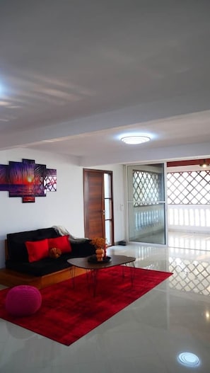 A modern living room with a black sofa, red cushions, a round coffee table, and a red rug.