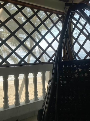 A balcony with a lattice railing, a view of the beach, and a palm tree.