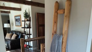 A wooden ladder leaning against a wall in a hallway with wooden flooring and a staircase. - Troullier's River House

 (White Lake)
