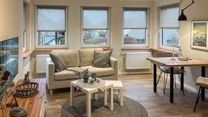 En moderne stue med sofa, spisebord og udsigt til det frie gennem store vinduer.