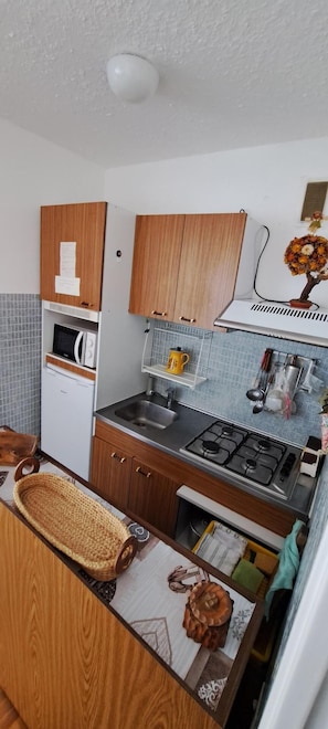 Pieni, käytännöllinen keittiö, jossa on puukaapit, mikroaaltouuni, kaasuliesi ja pesuallas.