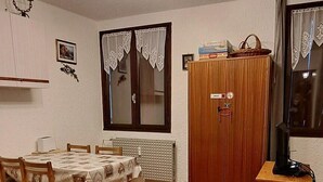 Una stanza con pavimento in legno, un tavolo da pranzo con sedie, un armadietto in legno, una televisione su un mobiletto in legno e una ventola a soffitto con luci.