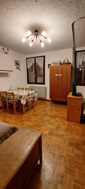 Huoneessa on puulattia, ruokapöytä tuoleineen, puinen kaappi, televisio puujalustalla ja kattotuuletin, jossa on valot.