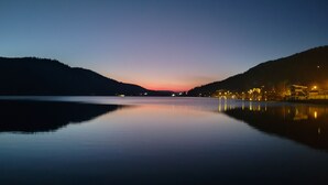 A calm lake at dusk with a sunset and a distant shoreline with buildings.