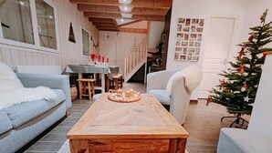 A cozy living room with a wooden coffee table, a blue sofa, a white armchair, and a decorated Christmas tree.