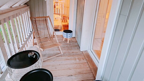 A wooden deck with a sloped ceiling, a wooden chair, a small round table, and a patterned stool.