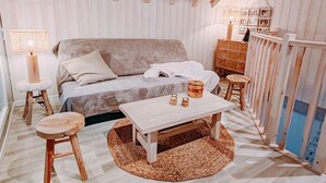 A cozy room with a wooden ceiling, a bed, a small table with candles, and a stool.