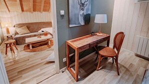 A cozy room with a wooden ceiling, a bed, a desk with a chair, a lamp, and a wall-mounted picture of a deer.
