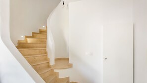 Eine Treppe mit beigen Stufen führt zu einer Zwischenebene, an den Wänden sind weiße Flächen zu sehen und darüber hängt eine Leuchte.
