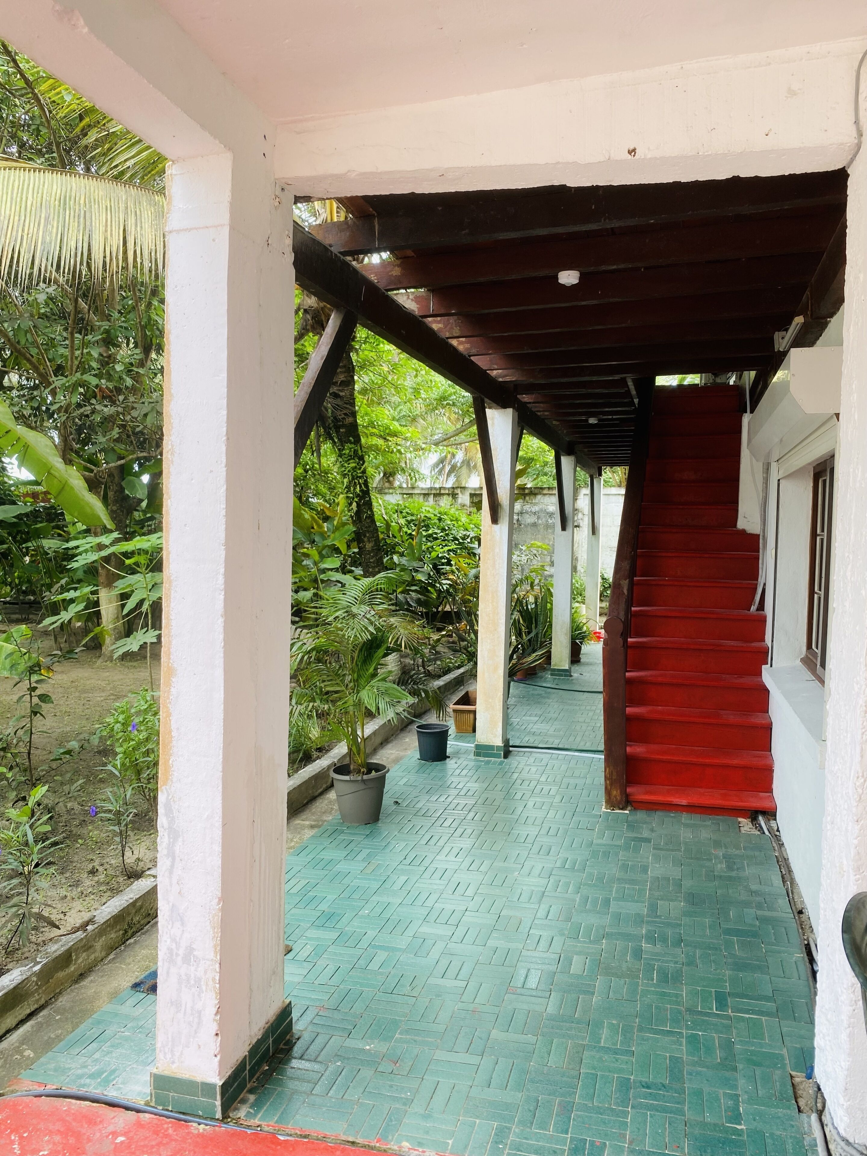 A covered outdoor corridor with a red carpet leading to a staircase.