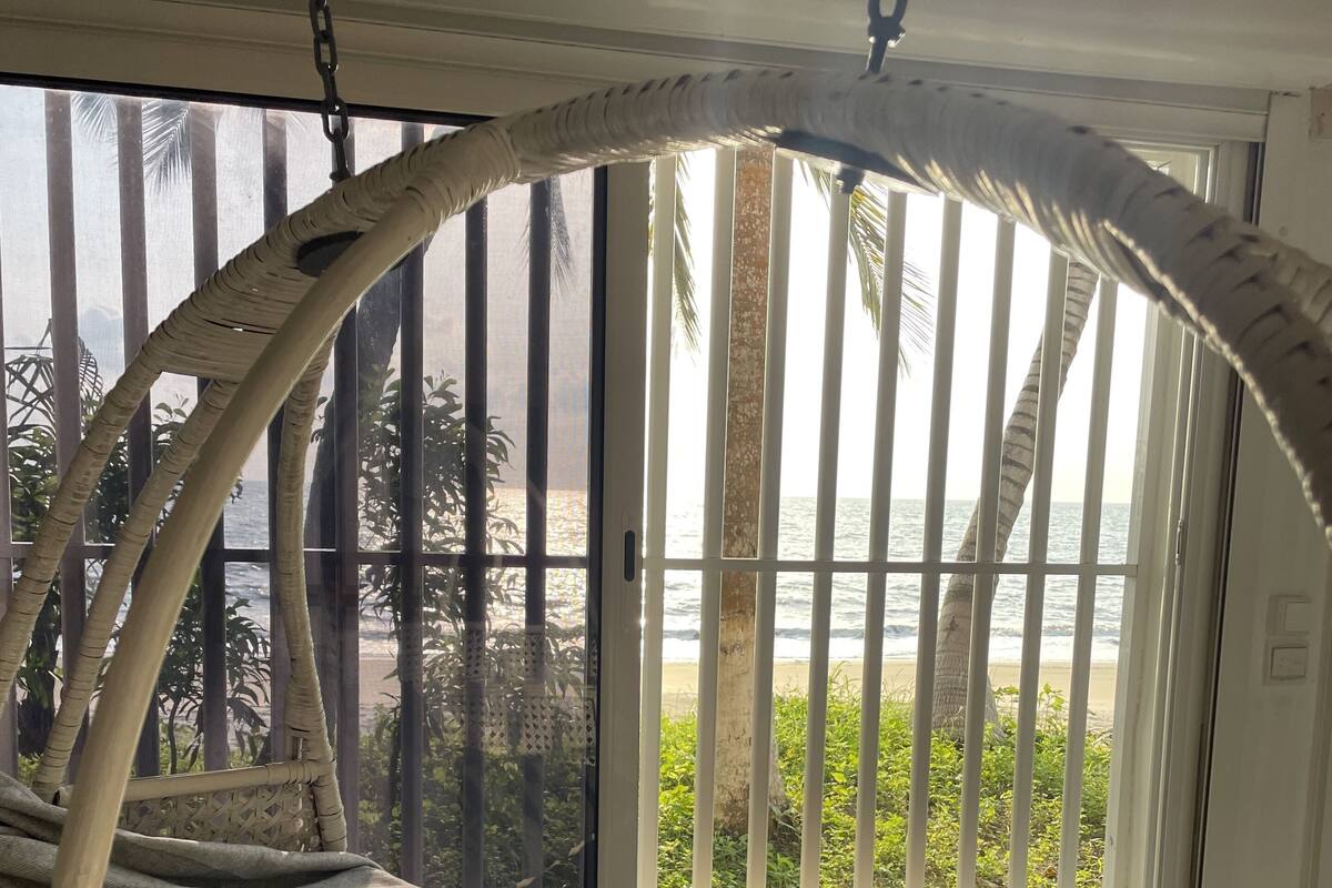A room with a large window offering a view of the beach and palm trees.