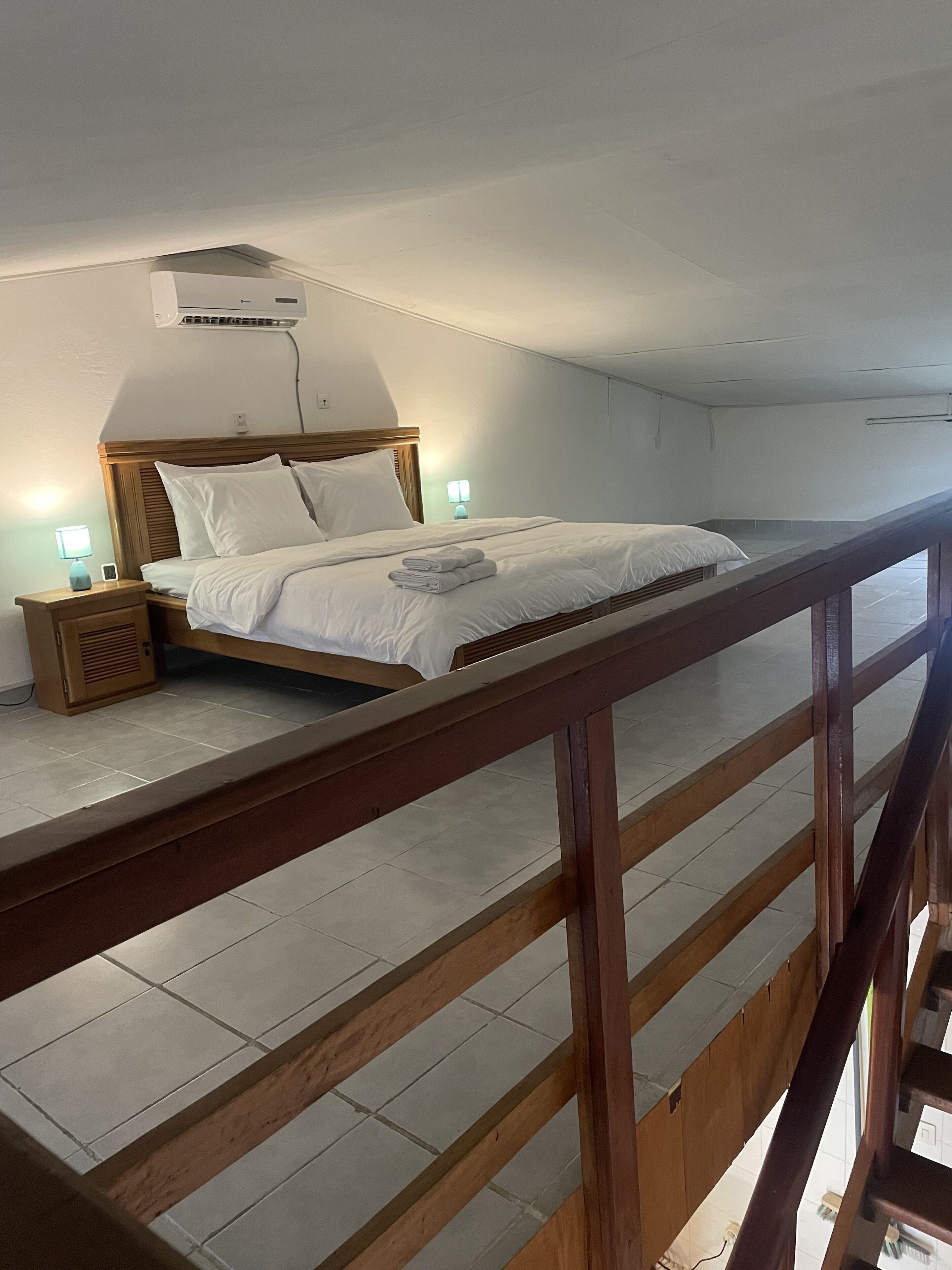 A hotel room with a wooden bed, a nightstand with a lamp, and a view of the outside through a window.