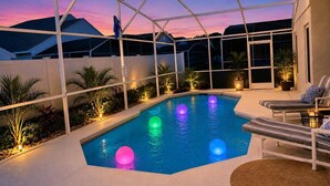 Una piscina con cerramiento de vidrio, rodeada de sillones de descanso y plantas en macetas.