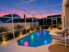 Una piscina con cerramiento de vidrio, rodeada de sillones de descanso y plantas en macetas.