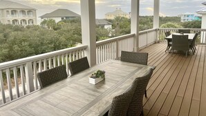 Un espacio al aire libre cubierto con piso de madera, una mesa de comedor con sillas y vistas a edificios y vegetación circundantes.
