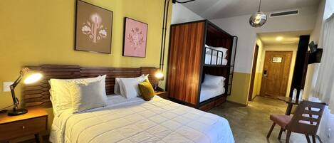 A hotel room with a bed, bedside lamps, a bunk bed, a desk, and a chair.