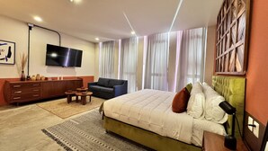 Una habitación de hotel moderna con una cama grande, un sofá, un televisor y un panel decorativo en la pared.