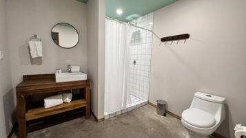 Un baño con tocador de madera, inodoro blanco, ducha con cortina blanca y un espejo redondo en la pared.
