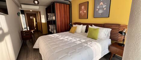 Una habitación de hotel moderna con una cama grande, cabecera de madera y una pared de acento amarilla.