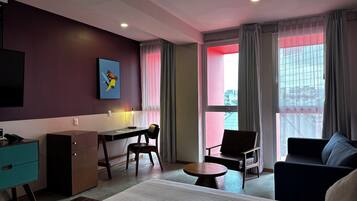 Ein modernes Hotelzimmer mit Bett, Schreibtisch, Stuhl, Sofa und Fernseher.