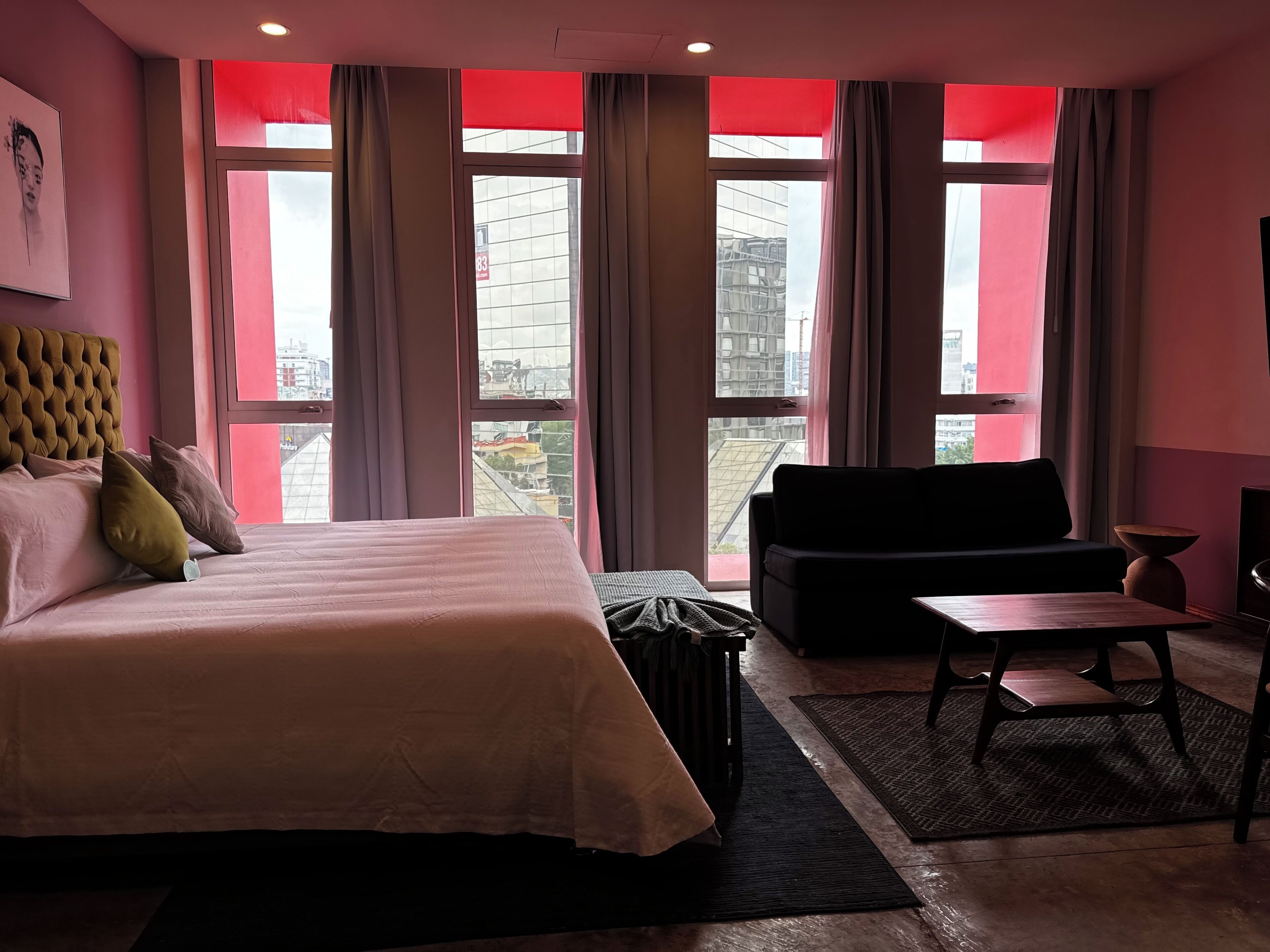 Ein Hotelzimmer mit einem großen Bett, einer schwarzen Couch, einem kleinen Tisch und Blick auf die Stadt durch große Fenster.