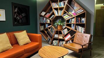 Un salon moderne avec une bibliothèque hexagonale remplie de livres, un canapé orange, un fauteuil en cuir marron et une table basse en bois.