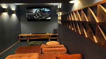 Un cine en casa con una televisión de pantalla plana grande montada en la pared, bancos de madera y cómodos asientos naranja.