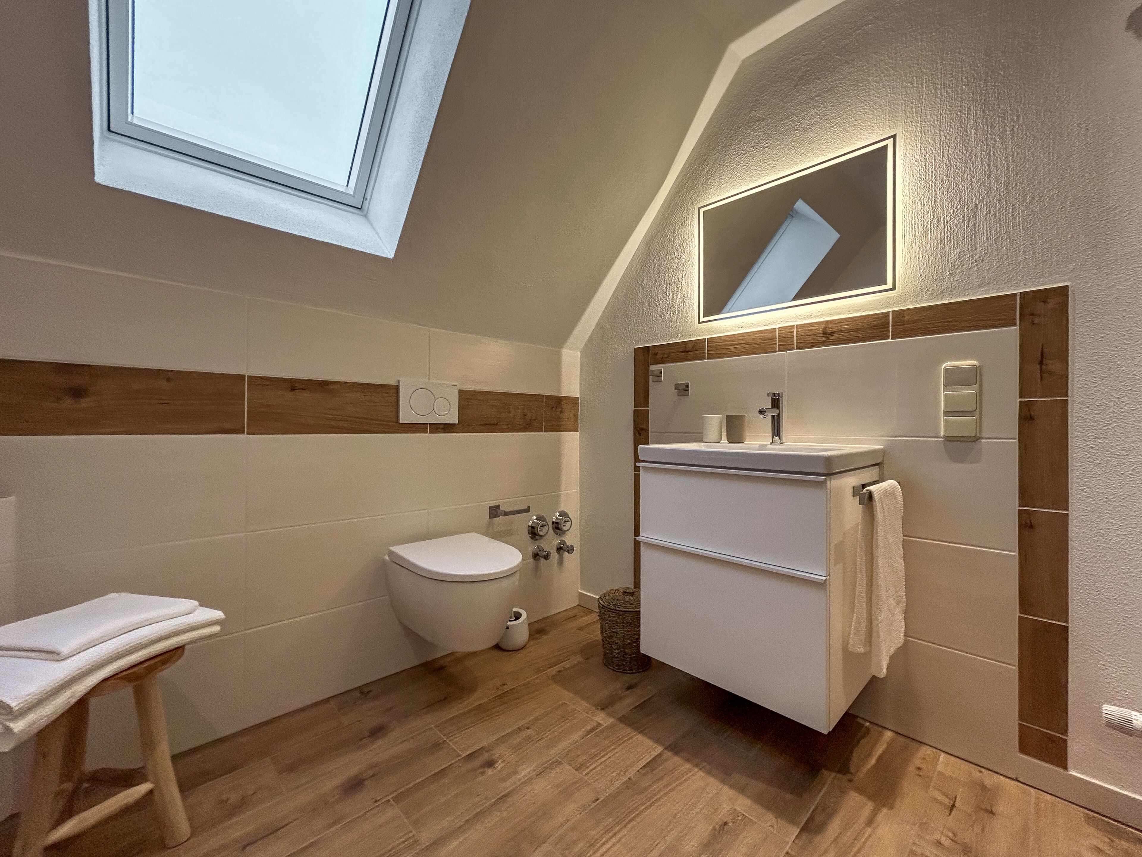Een moderne badkamer met dakraam, toilet, wastafel met handdoek en houten vloer.