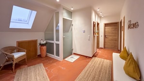 A modern interior with a sloped ceiling, a seating area with a sofa and cushions, a wicker chair, a potted plant, and a wooden door. - Beautiful, spacious holiday apartment in Neroth (Neroth)