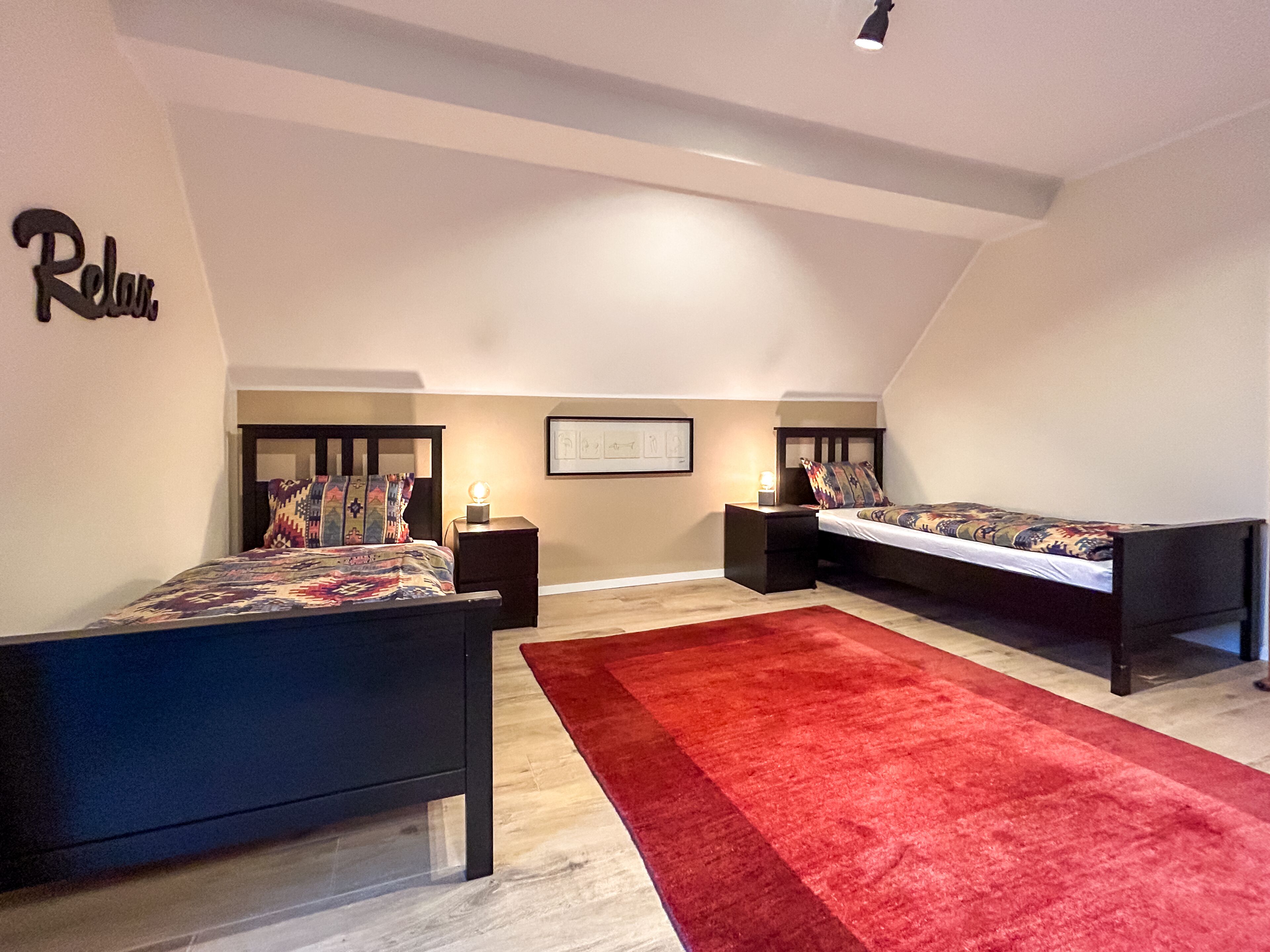 A bedroom with two beds, a red carpet, and a 'Relax' sign on the wall.