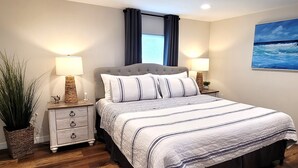 A bedroom with a large bed, two bedside tables, a potted plant, and a painting on the wall. - Land Lovers & Pirates Welcome #3 (Port St. Joe)
