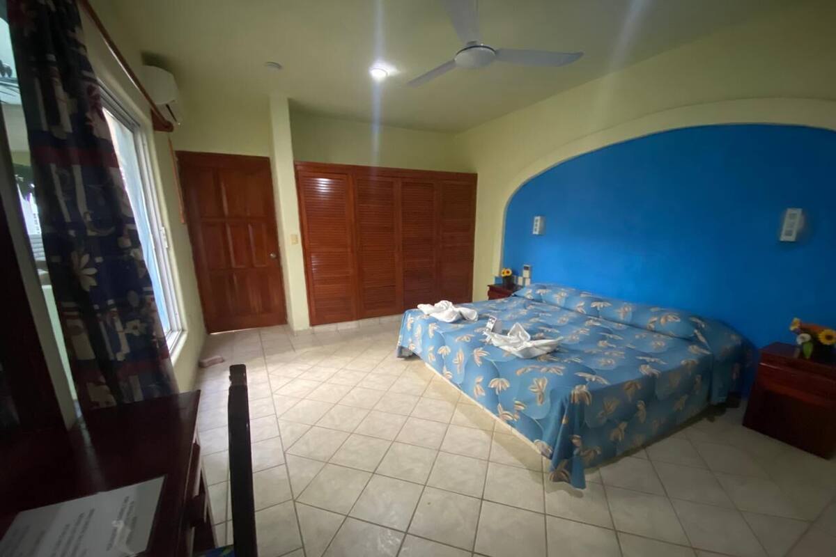Un dormitorio con cama, escritorio, silla, armario y ventana con cortinas.