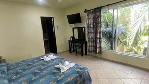 A hotel room with a bed, a desk, a chair, a TV, and a large window with curtains.