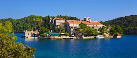 Um edifício histórico com uma torre, localizado às margens de um lago de águas azuis e vegetação exuberante.