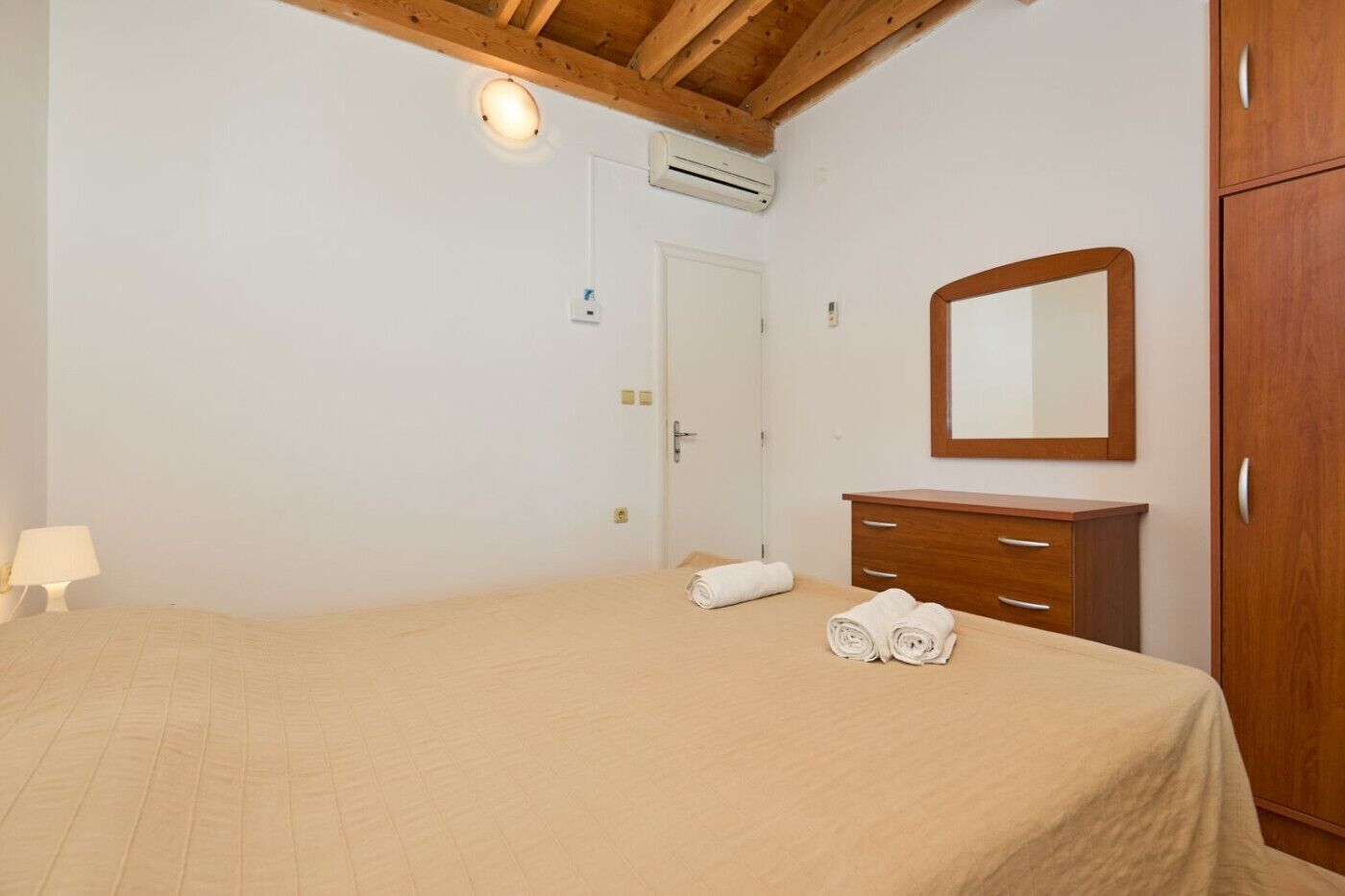 A bedroom with a bed, a wooden wardrobe, a mirror, and a door.