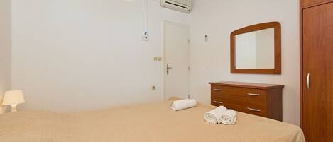 A bedroom with a bed, a wooden wardrobe, a mirror, and a door.