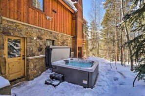 Eine Holzhütte mit Steinunterbau, einem Whirlpool und verschneitem Gelände.