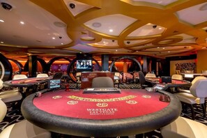 Ein Casino mit mehreren Blackjack-Tischen, einem großen Bildschirm, der ein Spiel zeigt, und einem markanten Deckenstil.