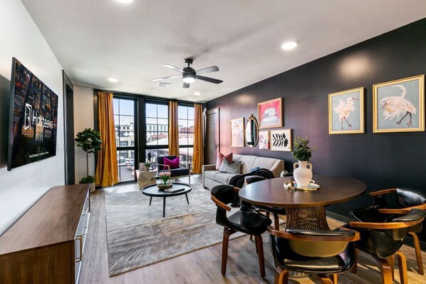 A modern living room with a round dining table, black chairs, a sofa, and a ceiling fan.