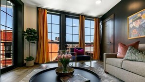 A modern living room with a large window, a round coffee table, a sofa, and a painting on the wall.
