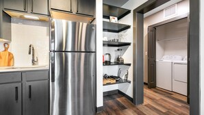 Une cuisine moderne avec un réfrigérateur en acier inoxydable, des meubles de couleur sombre et un plancher en bois.