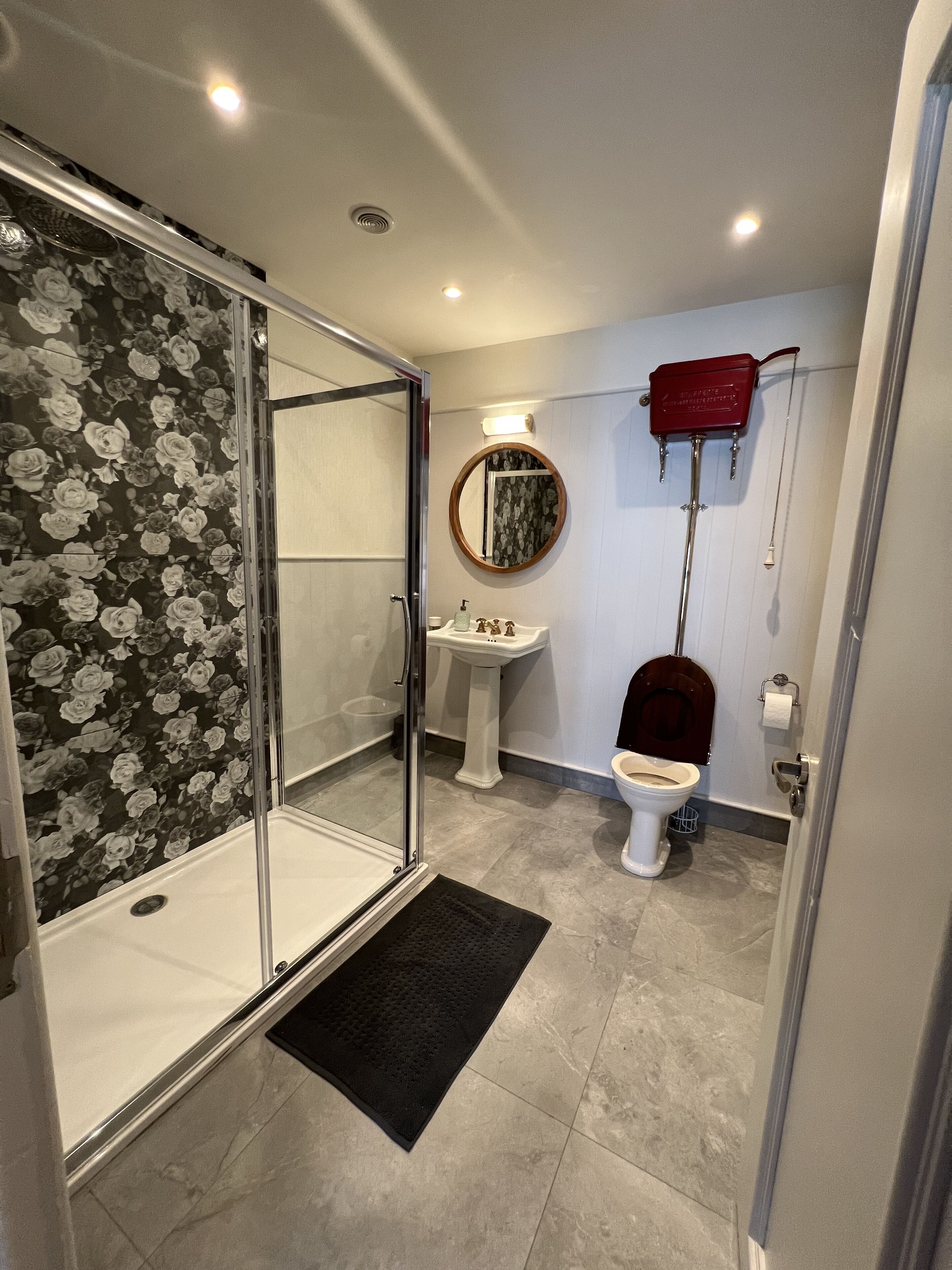 Ein Badezimmer mit Duschkabine aus Glas, einem Standwaschbecken, einer Toilette und einem roten Handtuchhalter.